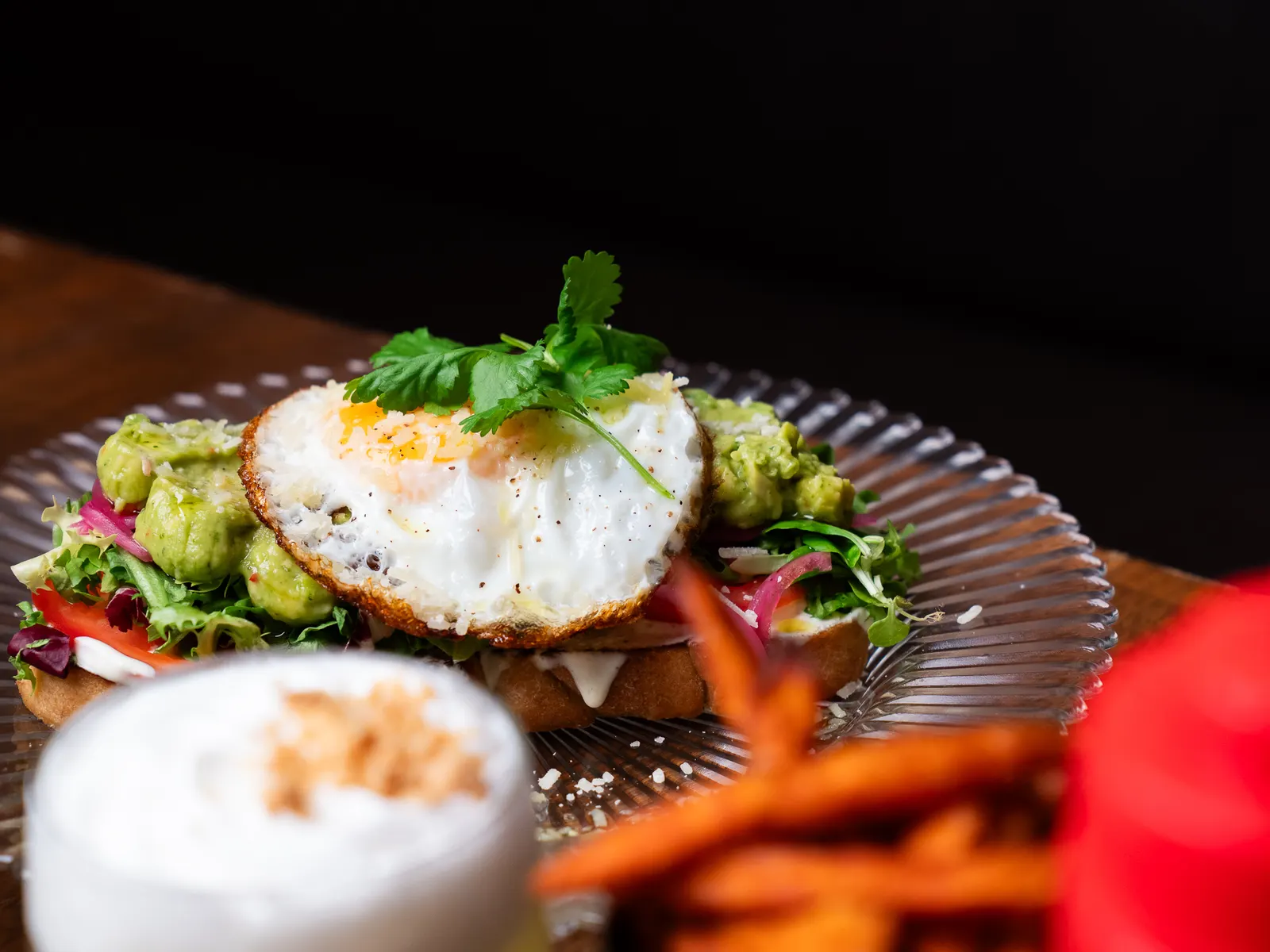 Avokadotoast med stekt ägg och koriander, serverad med pommes och en sour