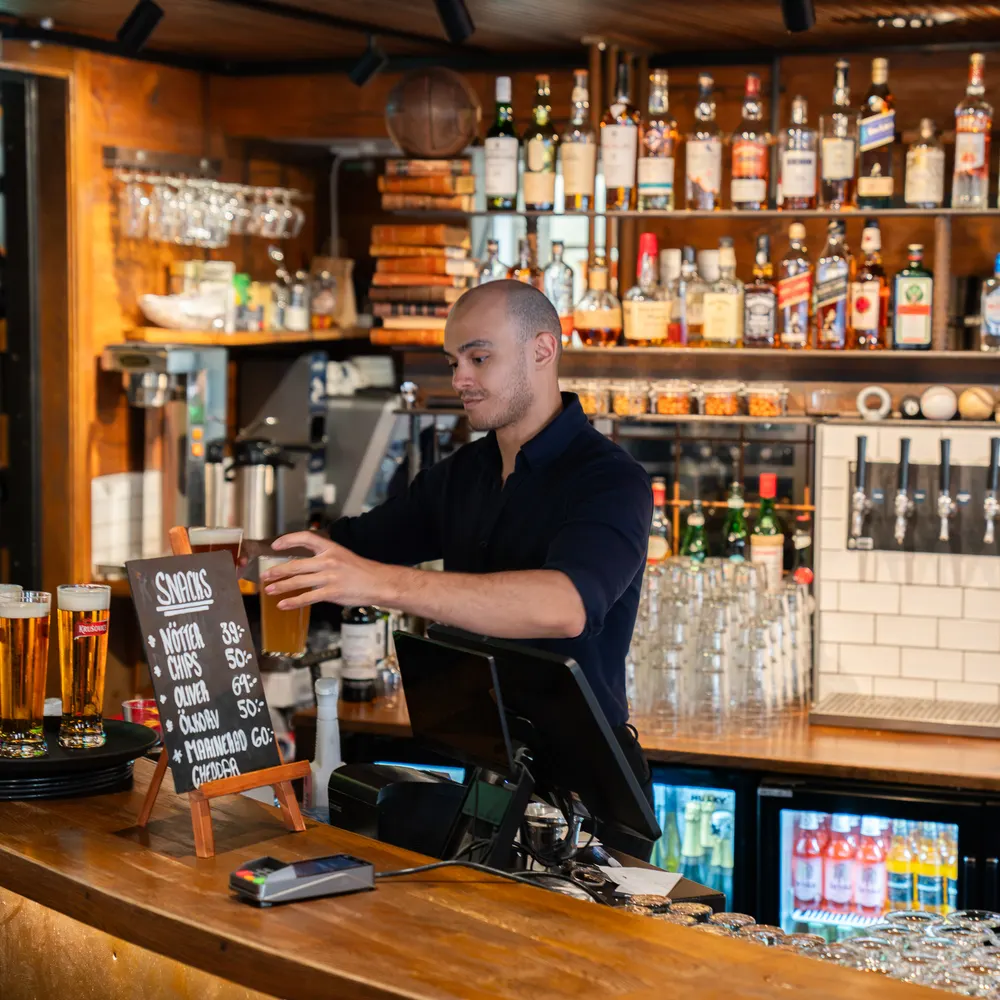 Bartender som tappar öl bakom baren med hyllor fulla av flaskor
